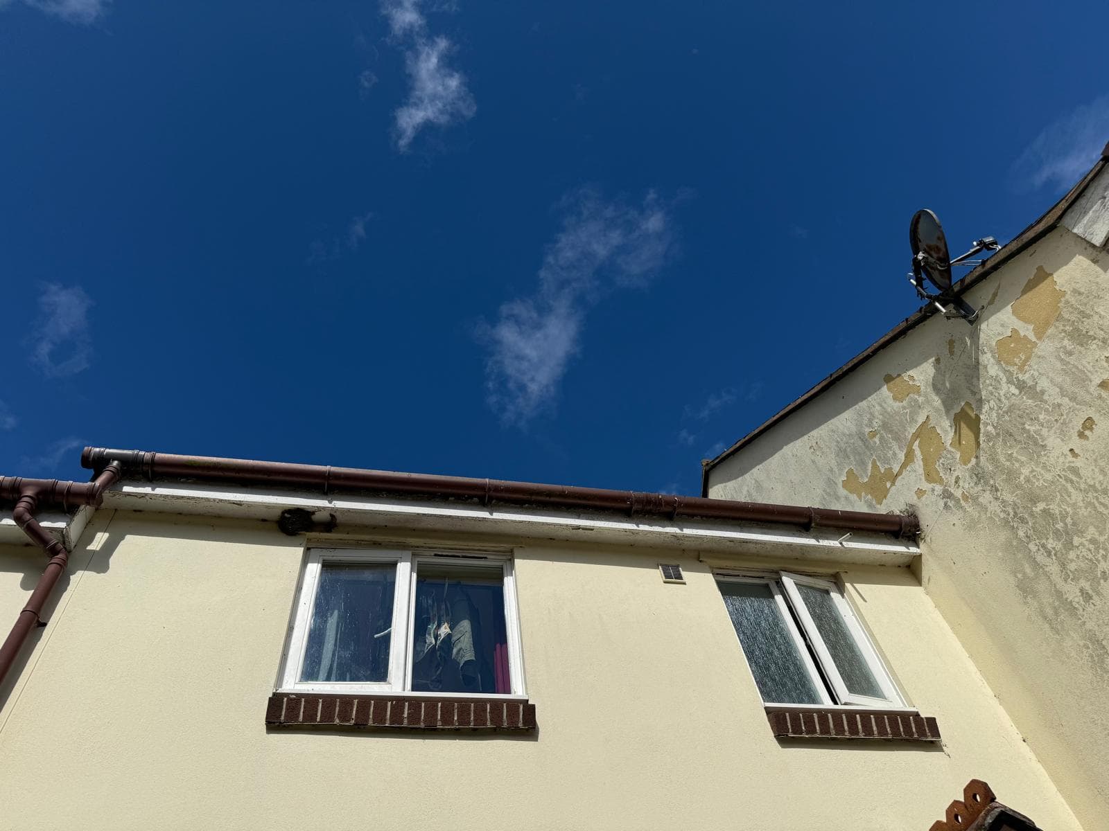Cleared brown guttering run along a cream rendered house under blue sky, Devon — Brixham