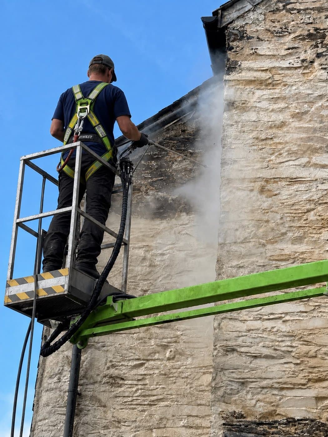 Moore & Franks operator DOFF steam-stripping failed paint back to bare stone on a Devon gable, working from a spider lift — Brixham