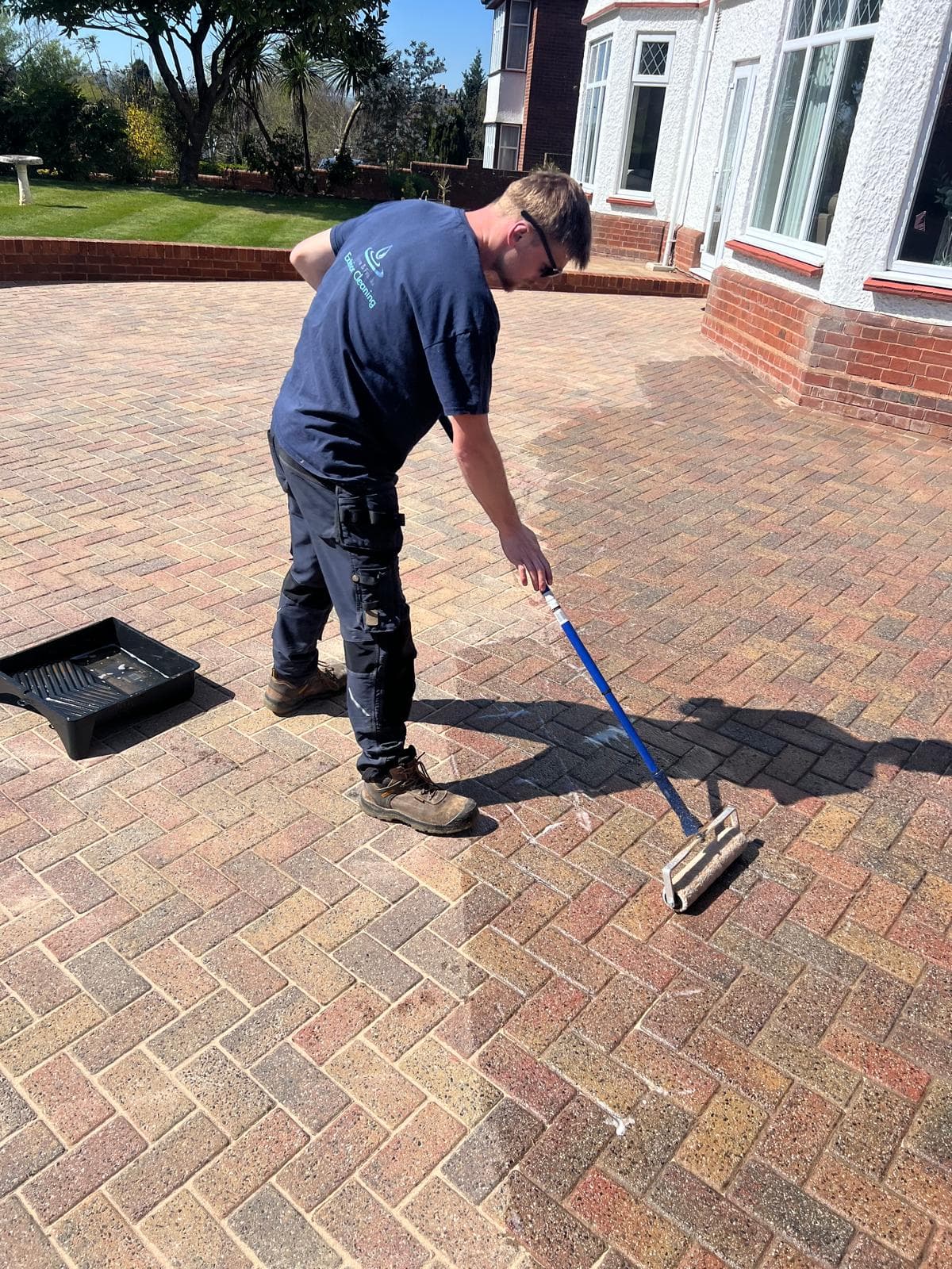 Operative brush-applying sealant to a block-paved driveway in front of a house, Devon — Cullompton