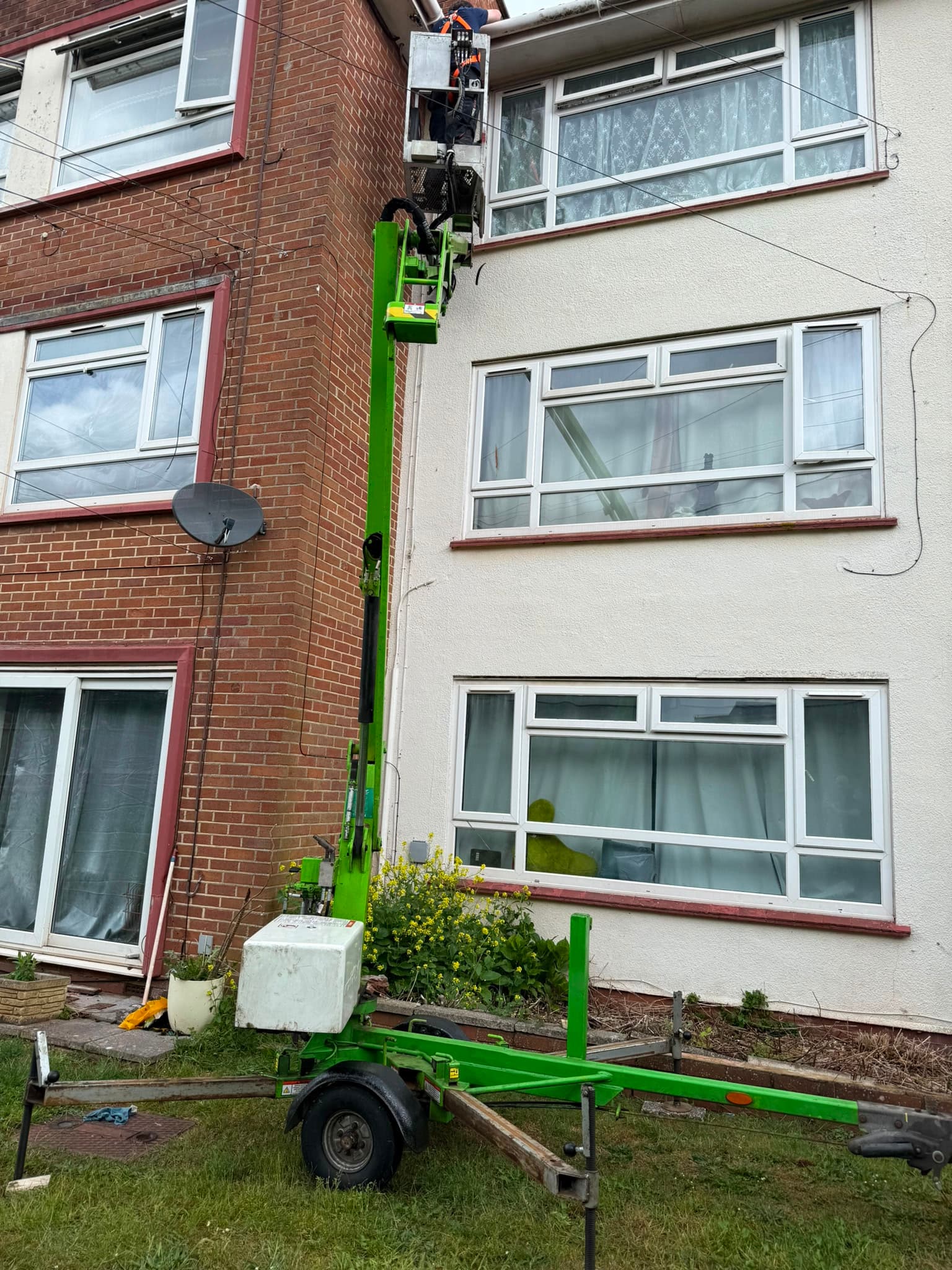 Operative on a cherry picker soft-washing the rendered elevation of a block of flats, Devon — Cullompton